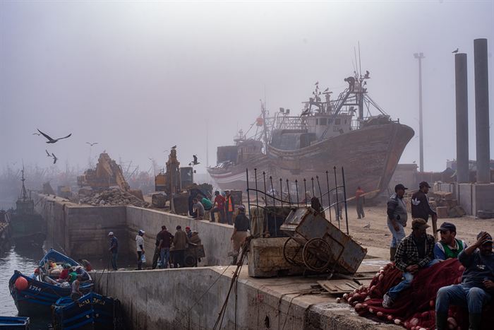 Fishermen and dockworkers among nets and crates in a misty working harbour, Morocco