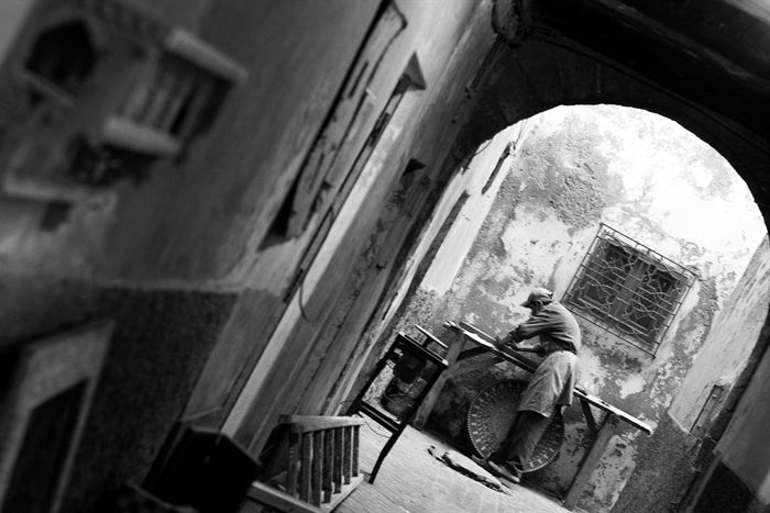 A craftsman working under a stone archway in a Moroccan medina, black and white