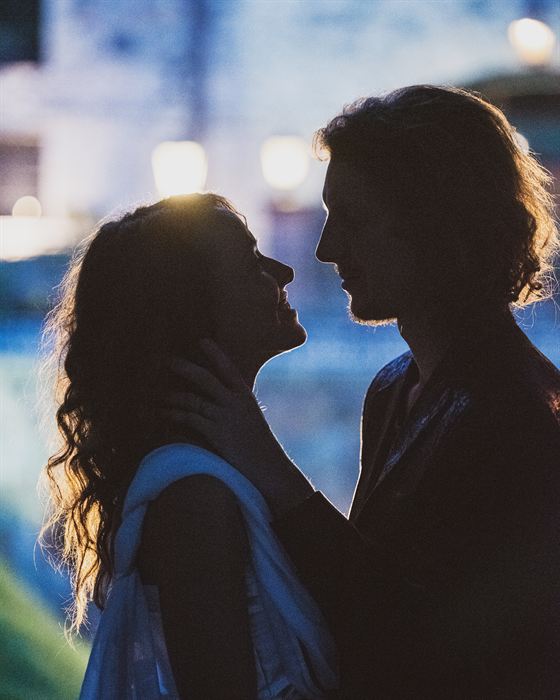 A couple facing each other in silhouette at blue hour, street lamps out of focus behind