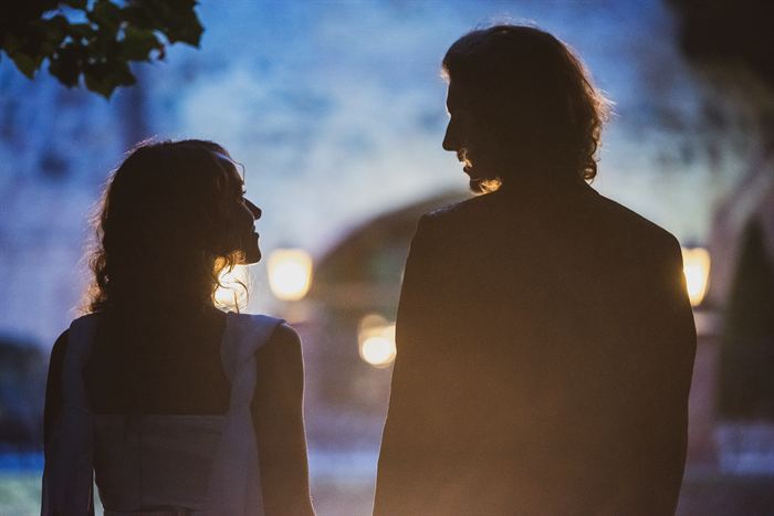 A couple standing close in silhouette against warm lamps at dusk