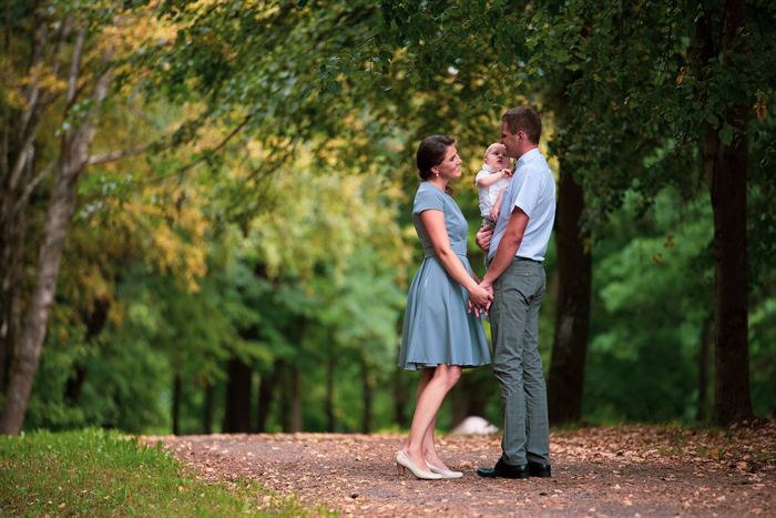 A couple holding a baby while standing on a tree-lined path in summer