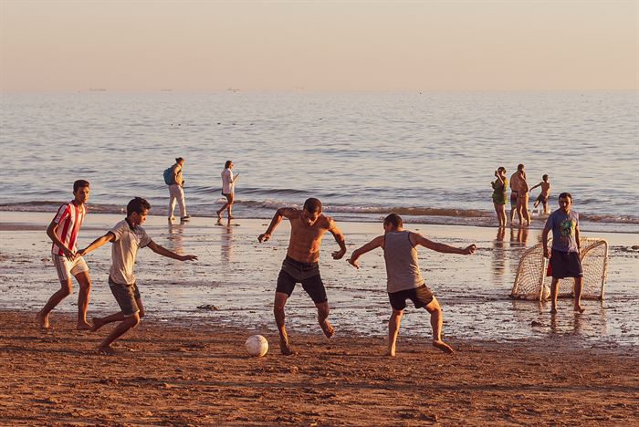 Young men playing football on wet sand at sunset