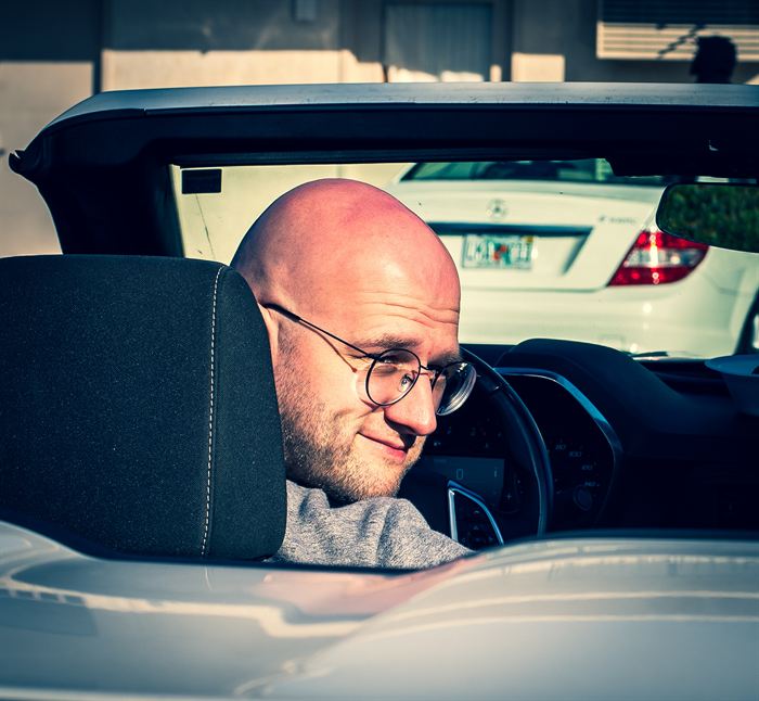 A man in glasses looking back over his shoulder from the seat of a convertible