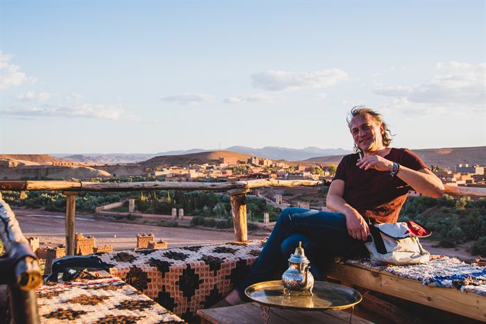 A man sitting on a terrace with mint tea, an earthen village and hills behind, Morocco
