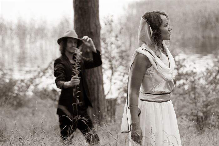 A man in a hat and a woman in white standing apart by a lake, sepia