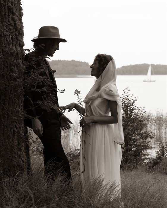 A couple standing beneath a tree by a lake with a sailboat on the water, sepia