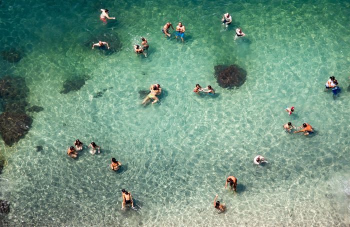 Swimmers seen from above in clear turquoise shallows over rock