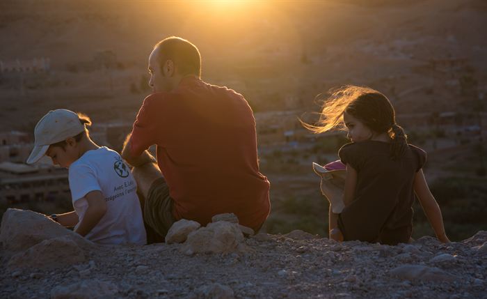 A man and two children sitting on a ridge at sunset, hair rimmed by the light, Morocco