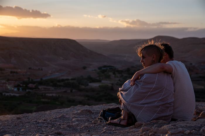 A couple sitting wrapped together watching sunset over a desert valley, Morocco