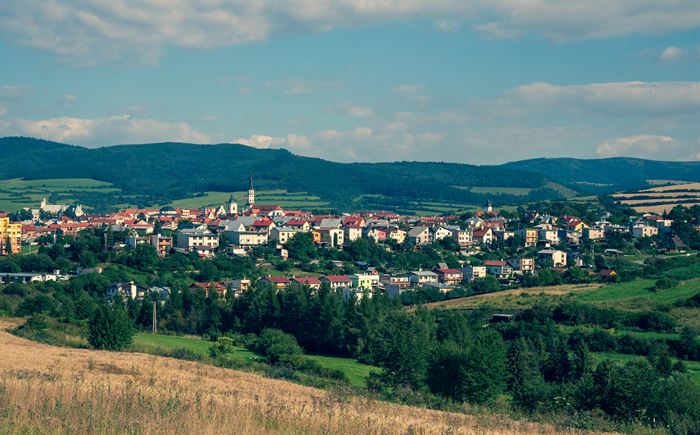 A small town with red tiled roofs spread along a green valley beneath wooded hills