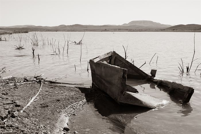 A half-sunken wooden boat at the edge of a shallow lake with dead branches standing in the water