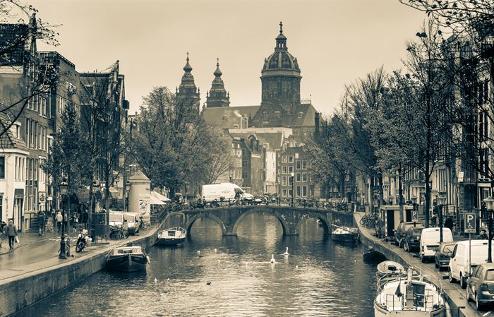 An Amsterdam canal lined with moored boats, a domed church closing the view, toned sepia