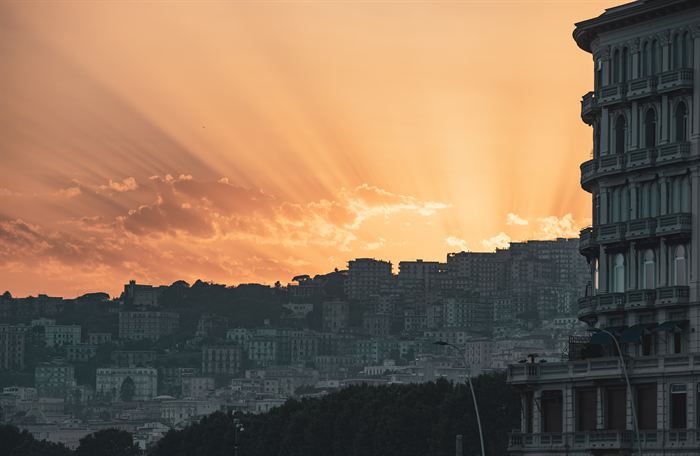 Sun rays breaking through cloud above the hillside apartment blocks of Naples, Italy