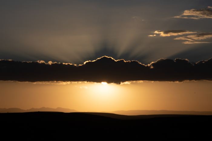 The sun setting behind a long bank of cloud over a dark desert horizon