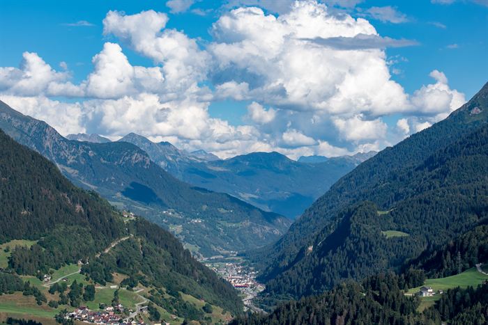 An alpine valley with a village on the floor far below, under tall summer cumulus