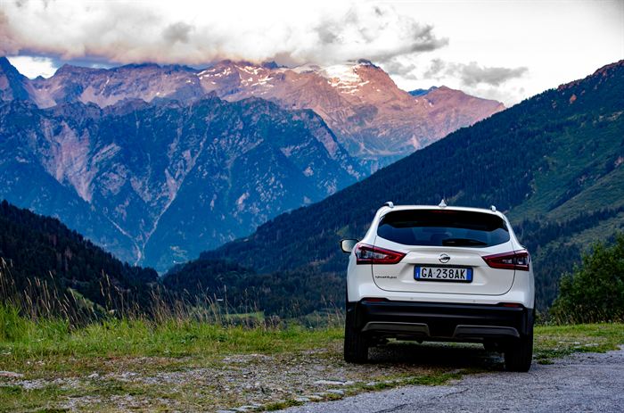 A white car parked at a viewpoint facing snow-lit alpine peaks at dusk