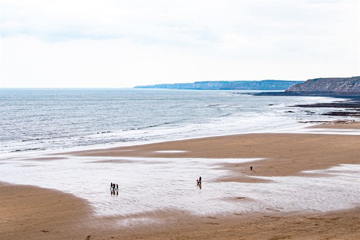 A wide sandy beach at low tide with distant cliffs and a few small figures