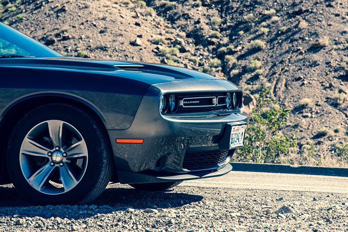 The front of a dark Dodge Challenger parked against a bare desert slope