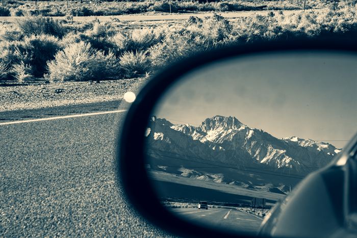 Snow-capped mountains reflected in a car wing mirror above a desert roadside