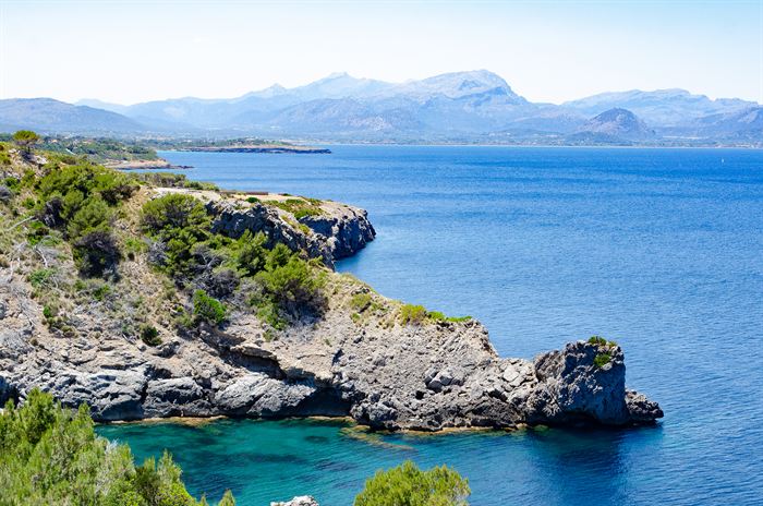A rocky Mediterranean bay with turquoise water and mountains along the far shore