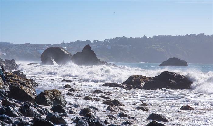 Waves breaking over dark rocks along a rugged coastline
