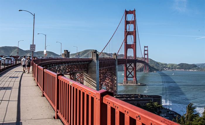 The walkway of the Golden Gate Bridge with its red railing running towards the tower
