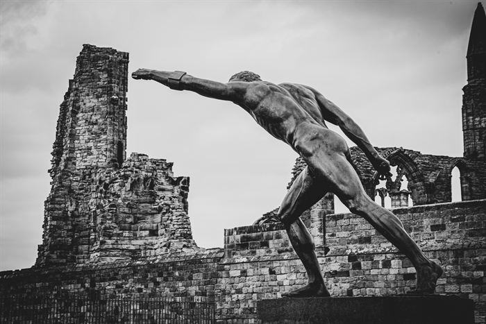 A bronze athlete statue against the ruins of an abbey, black and white