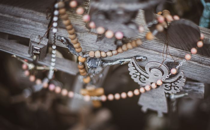 A rosary and a small metal angel among weathered wooden crosses, Hill of Crosses, Lithuania